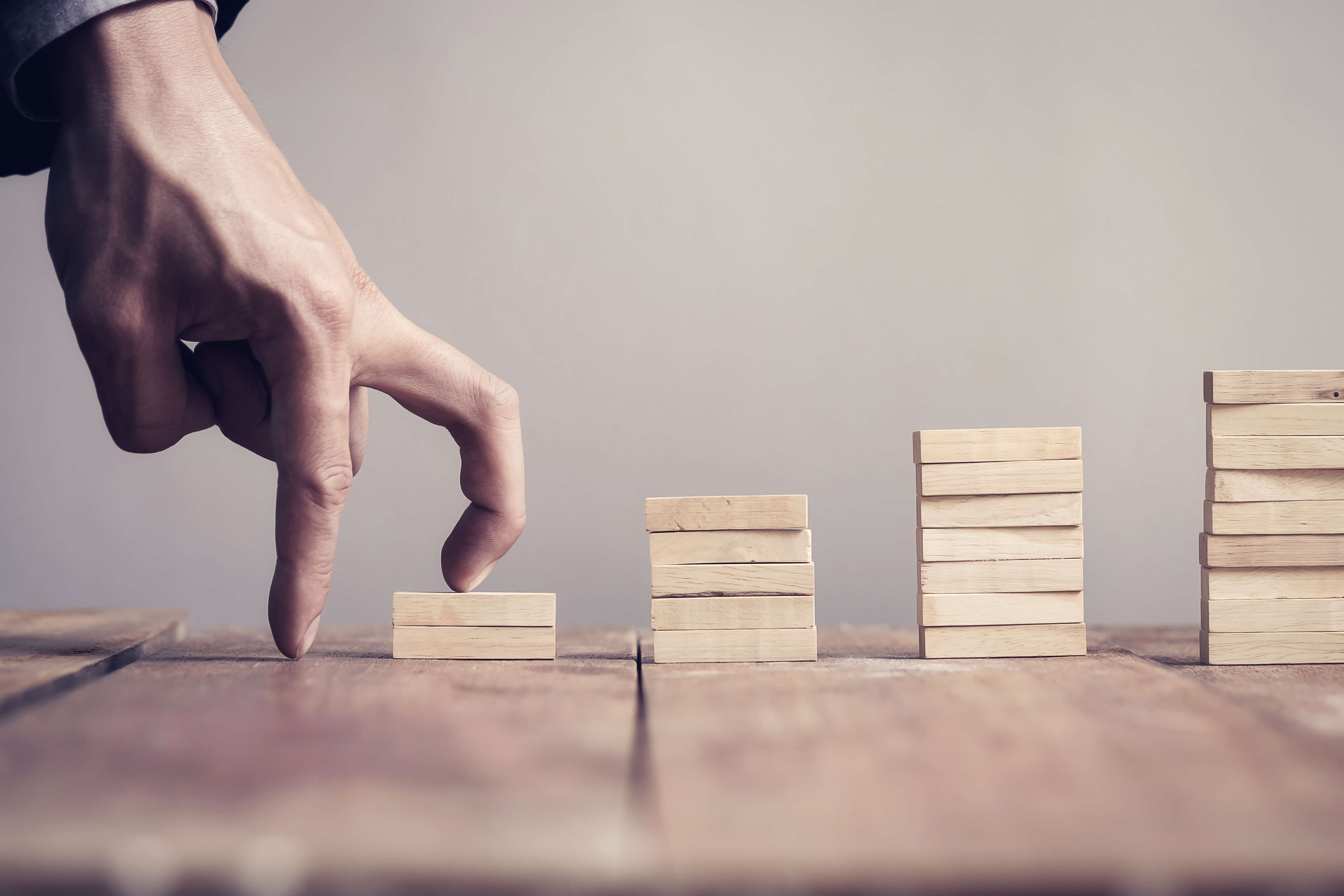 Hand of business man step up to a toy staircase to success target